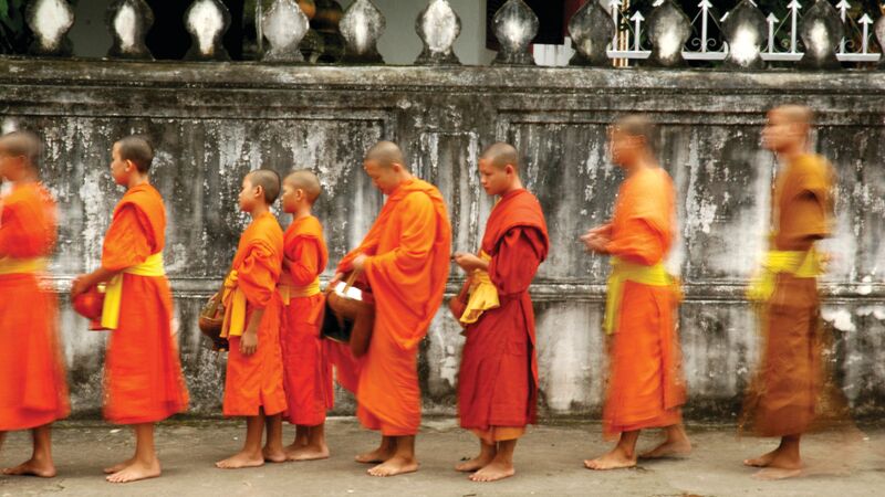 A group of orange-robed Monks lining up to receive Alms. 