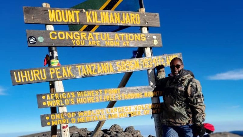 A woman stands in front of a sign on Mt Kilimanjaro