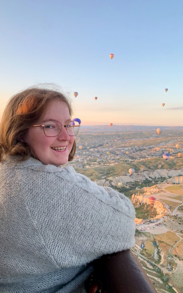 Woman watching hot-air balloons in Cappadocia smiles at the camera.