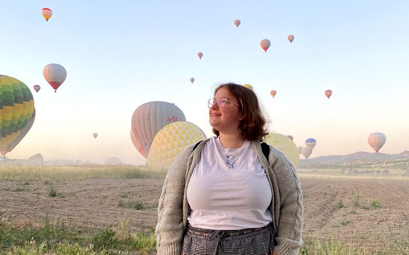 Woman backdropped by hot-air balloons at sunrise in Cappadocia, Turkey