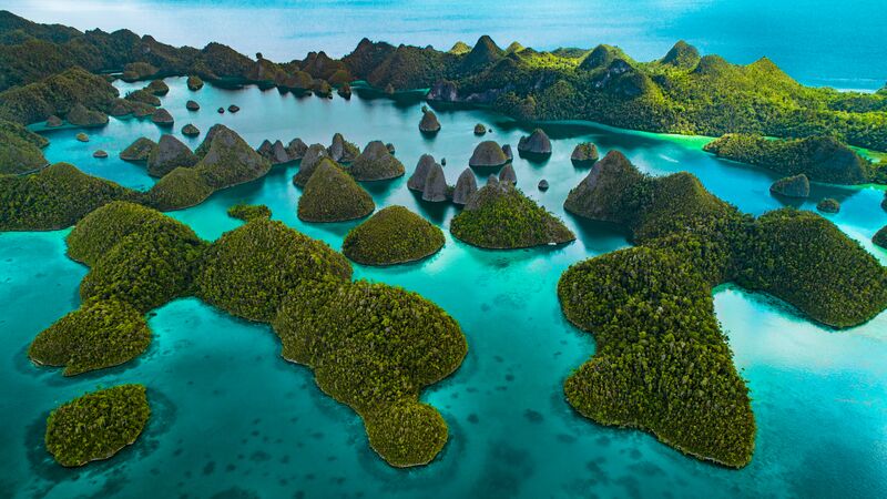 Aerial view of some of Indonesia's delicious islands, surrounded by blue water. 