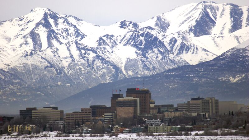 The city skyline of Anchorage with snow-capped mountain ranges in the background. 
