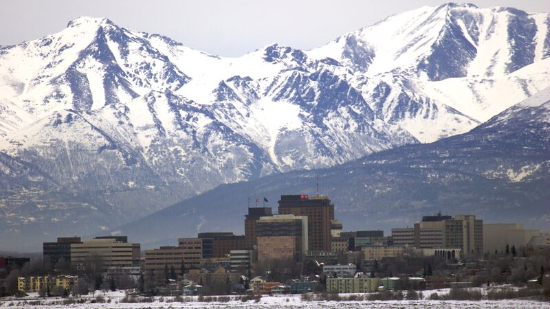 The city skyline of Anchorage with snow-capped mountain ranges in the background.
