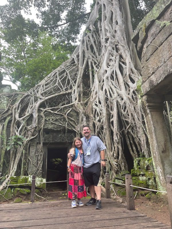 A father and daughter standing in front on an ancient tree and temple