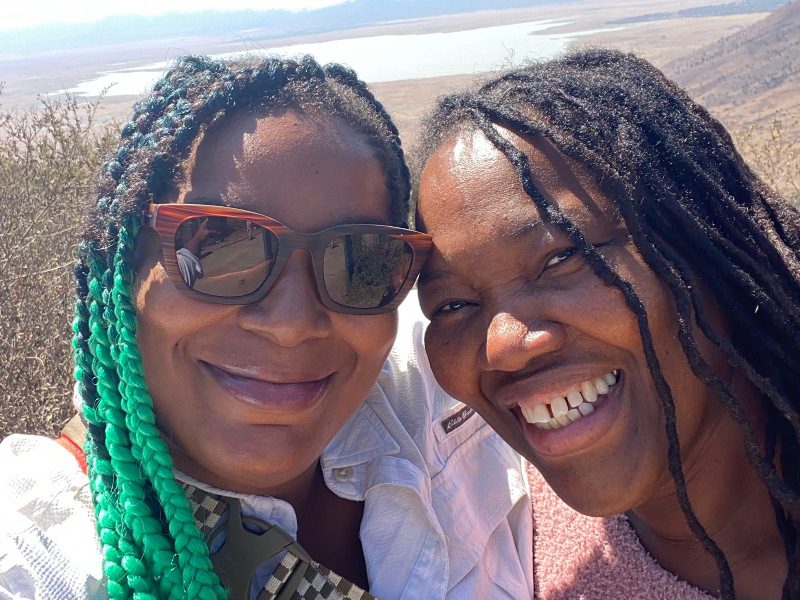 Two women, one wearing sunglasses, smile for a selfie