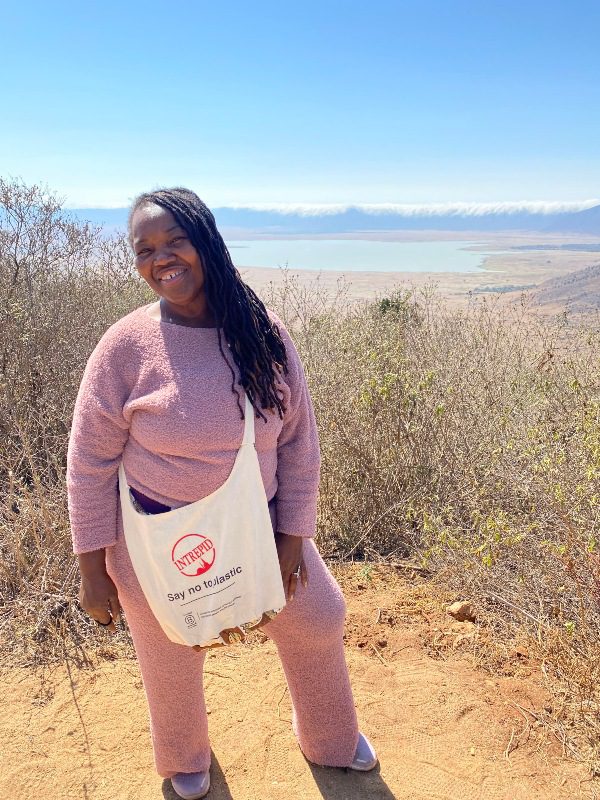 A woman wearing a pink tracksuit and an Intrepid tote bag poses in the Ngorongoro Crater