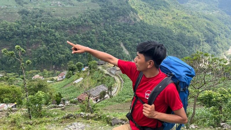 A man wearing a red tshirt and a backpack points into the distance