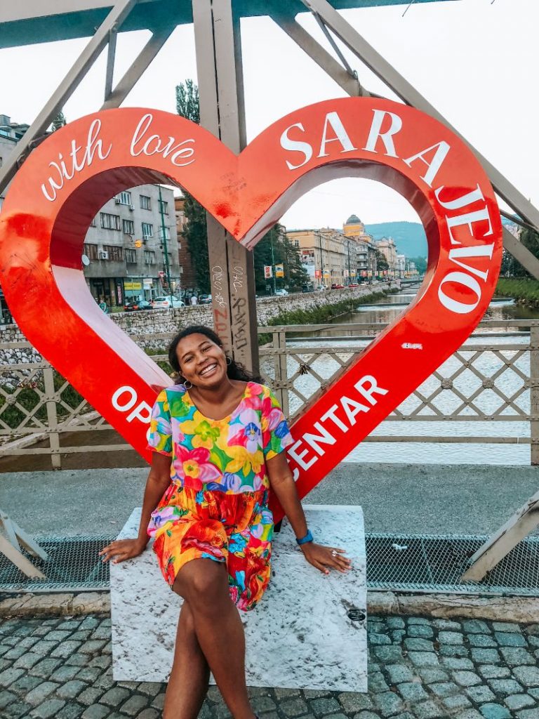 A girl wearing a brightly coloured dress sitting in front of a heart-shaped sign