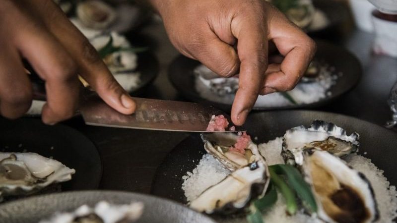 Close up of hands on a knife placing finger lime onto shucked oysters