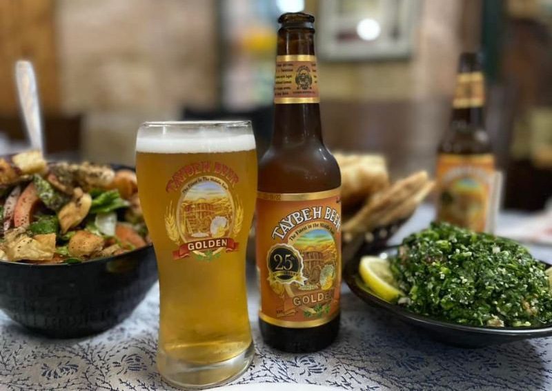 A glass and bottle of beer on a table alongside two salads