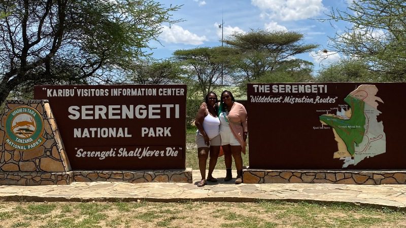 Two women standing in front of a Serengeti sign in Tanzania