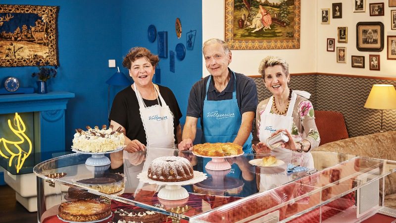 Three older staff members working at a cake shop. They are all smiling.