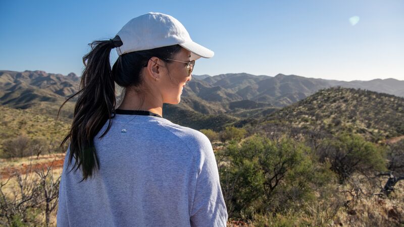 A woman wearing a white cap with a dark ponytail looks out over the Australian bush