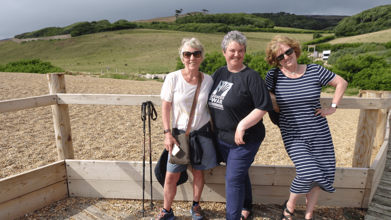 Three smiling women stand in from of rolling green hills in Dorset, UK