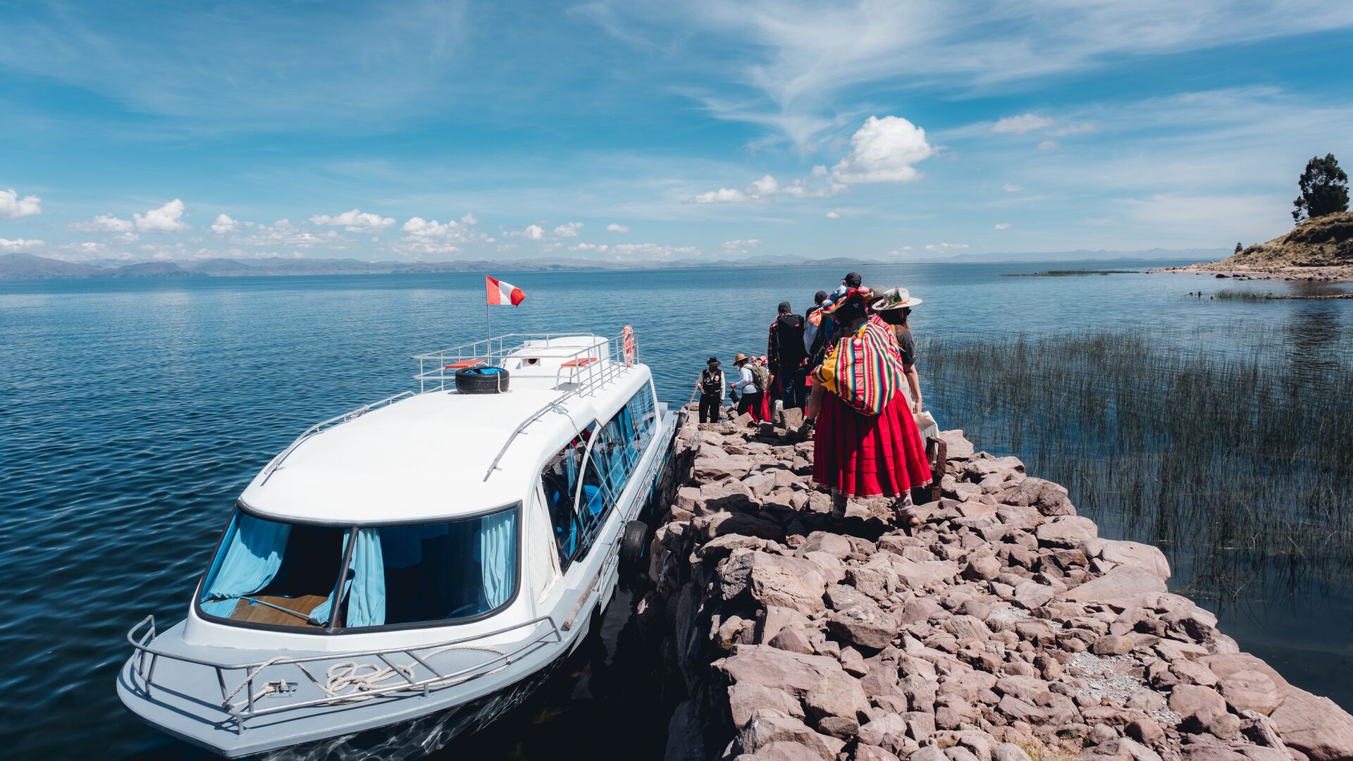 Travellers walking over a rocky pier to board a boat back to Puno after a Llachon homestay