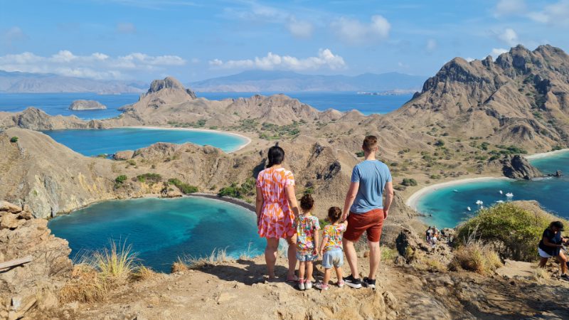 A couple hold hands with their two young children as they admire a viewpoint on Padar Island, Indonesia