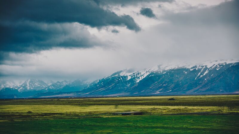 The vast green landscape of Iceland with stormy clouds and mountain ranges in the distance. 