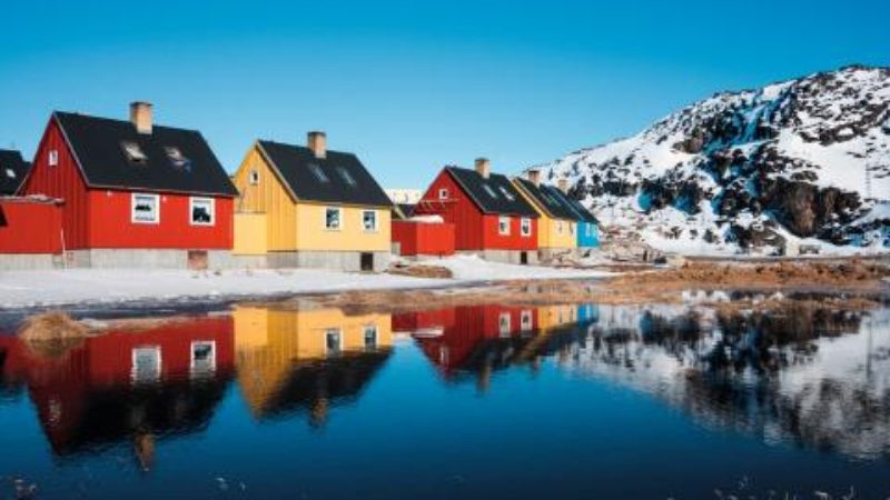 A row of brightly coloured houses on the banks of a mirror-like lake.