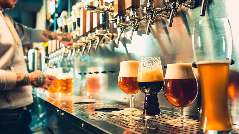 A couple of beers lined up under their taps while a man pours more.