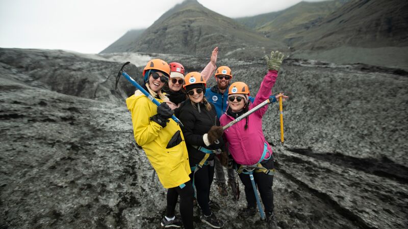 A group of travellers in brightly coloured jackets holding pick axes on a geyser in Iceland.