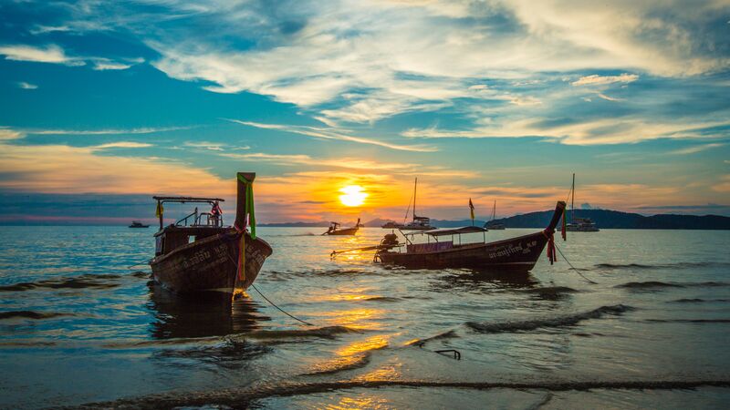 The sun setting behind two traditional wooden boats in Ao Nang, Thailand