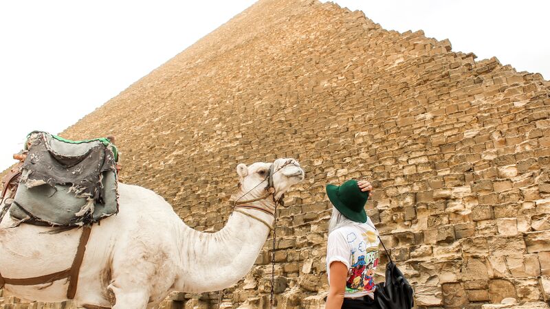 A traveller stares up at a Pyramid while standing next to a camel