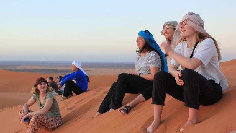 A group of travellers sitting on a sand dune in the middle of the Sahara Desert in Morocco.