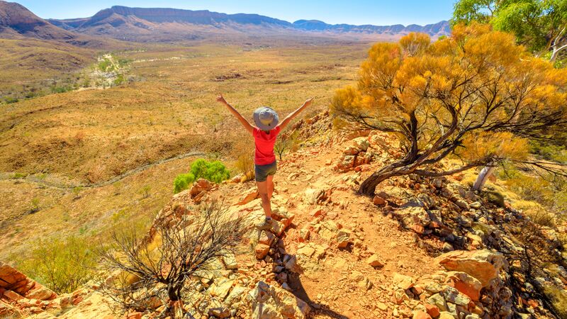 A hiker throwing their arms in the air with excitement on the Larapinta Trail in the Northern Territory, Australia