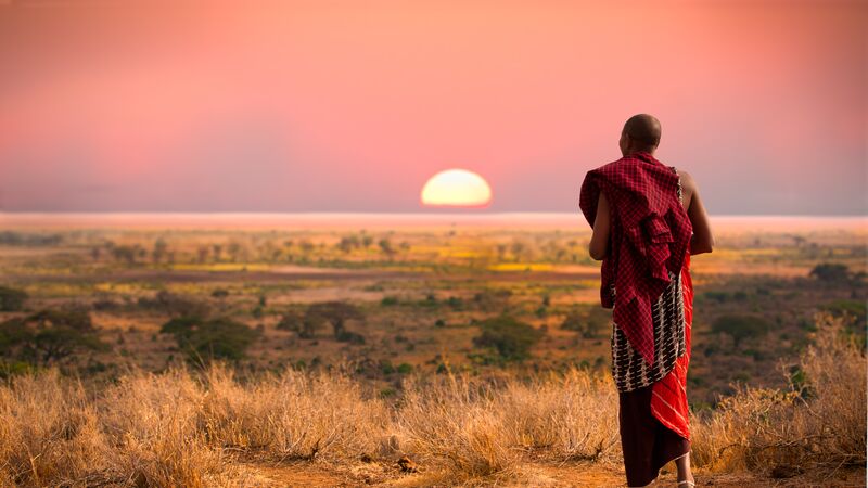 A local Maasai Mara man looking out over the Serengeti landscape at sunset. 