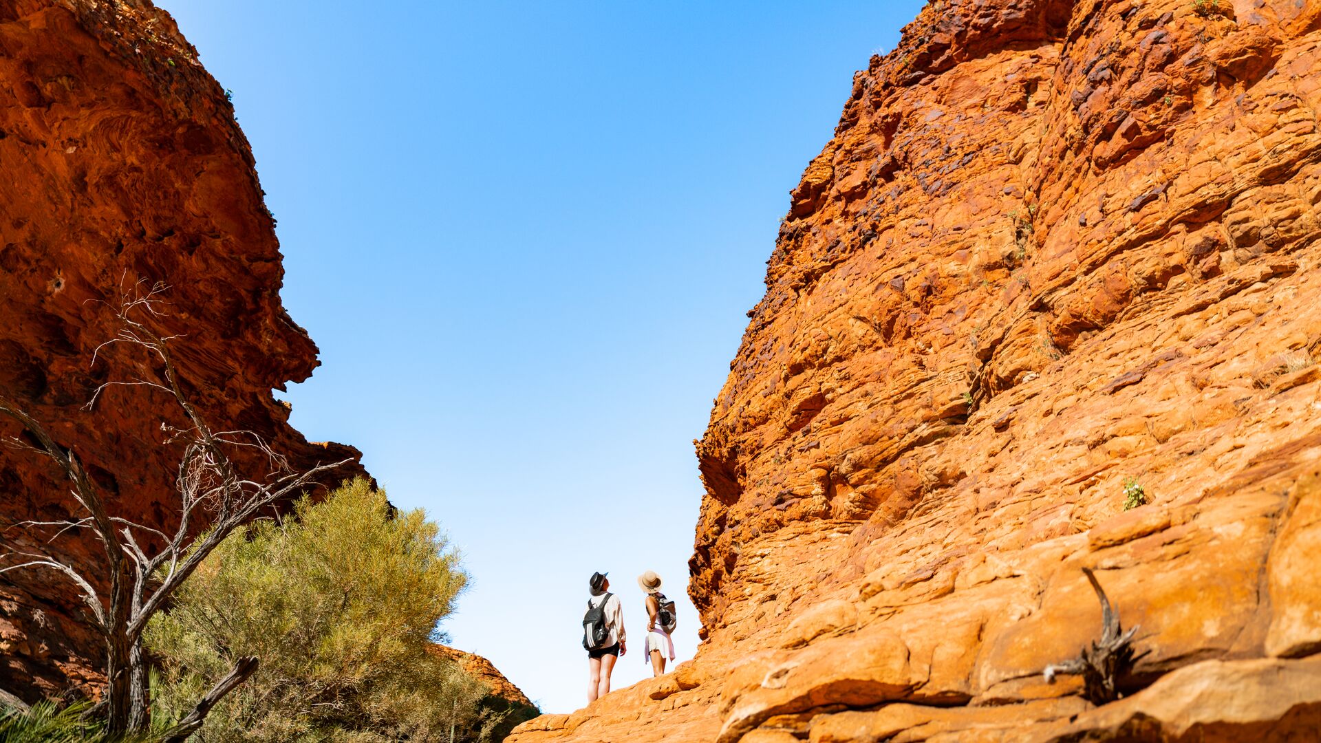 Two travellers stand looking up between two cliff walls in the Outback.