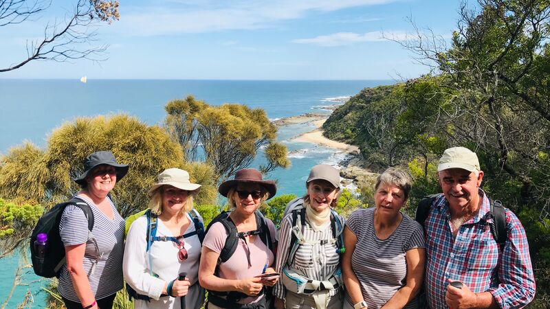 A group of travellers smiling at the camera in front of stunning coastal scenery as part of the Great Ocean Walk 