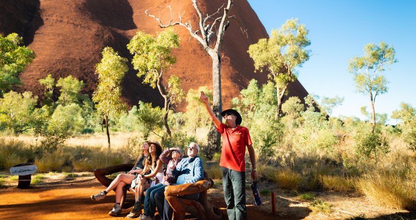 An Intrepid guide sharing information about Uluru to a group of four travellers