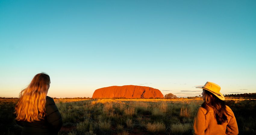 Two travellers admiring Uluru glowing at sunset