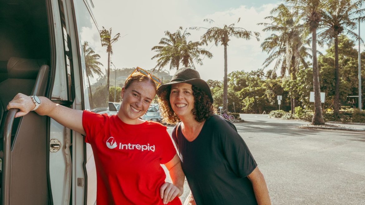 An Intrepid leader and traveller smile by a van with palm trees in the background.