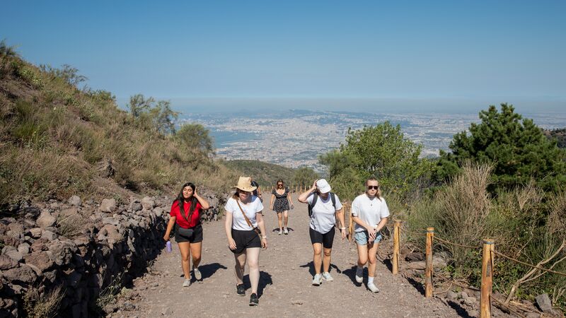 A group of travellers walking up a hill in italy under a clear sky.