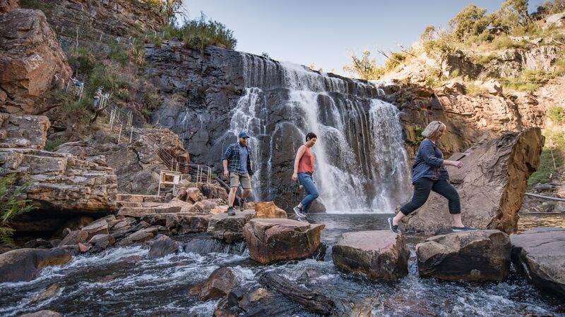 Three hikers walking across stepping stones at MacKenzie Falls in the Grampians