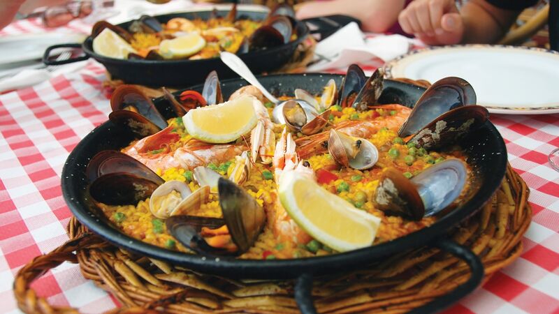 A bowl filled with seafood paella, sitting on a checkered tablecloth. 