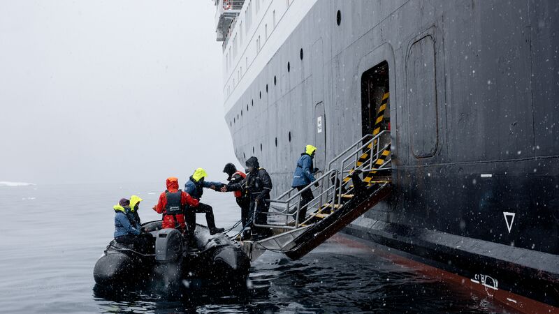 Ocean Endeavour crew members helping passengers off a zodiac boat in a snow storm. 