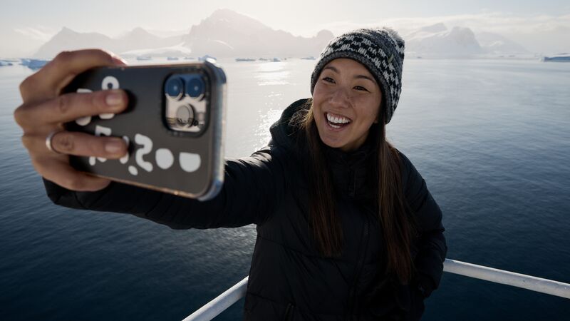 A solo woman traveller taking a selfie on the deck of the Ocean Endeavour with the Antarctic landscape in the background. 