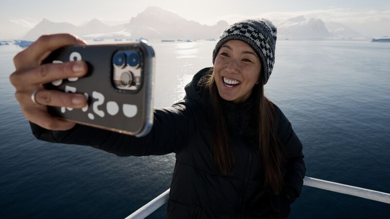 A solo woman traveller taking a selfie on the deck of the Ocean Endeavour with the Antarctic landscape in the background.
