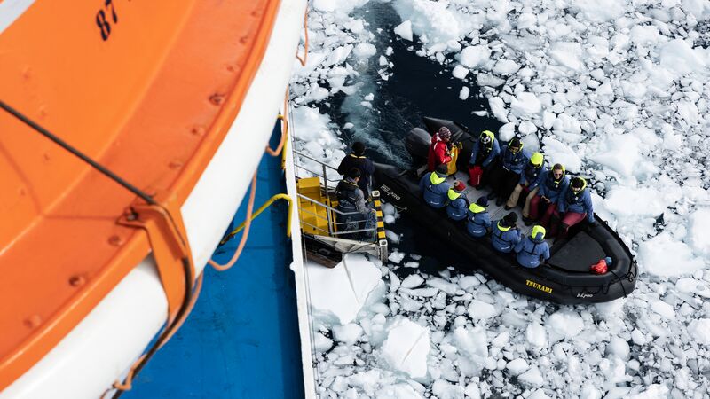 Aerial view of a zodiac boat full of passengers, bobbing in the icy ocean. 