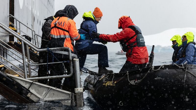 A couple of crew members helping a passengerfrom the Ocean Endeavour to a zodiac boat in Antarctica. 