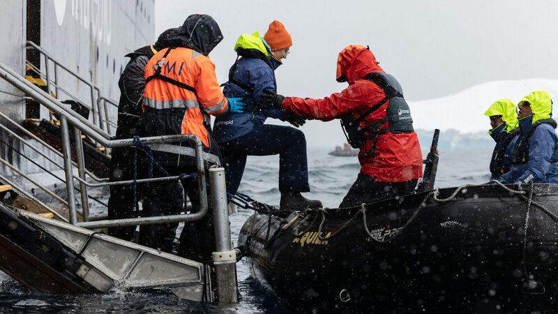 A couple of crew members helping a passengerfrom the Ocean Endeavour to a zodiac boat in Antarctica.