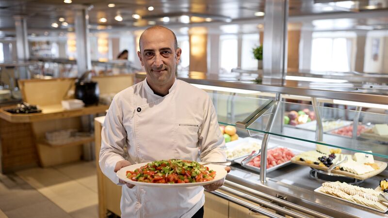 An onboard chef holding out a plate of food in the dining area. 