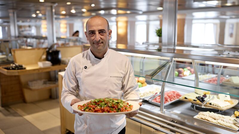 An onboard chef holding out a plate of food in the dining area.