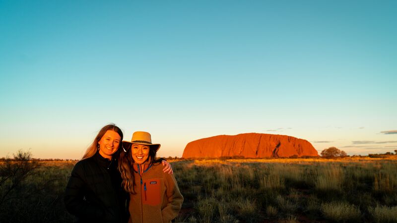 Two female travellers smiling for a photo at Uluru at sunset