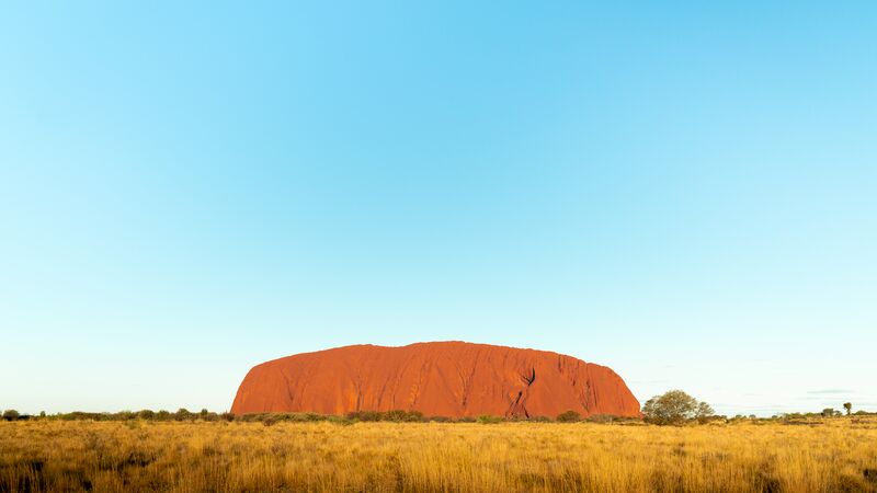The impressive and rust-coloured form of Uluru on a clear, blue day.