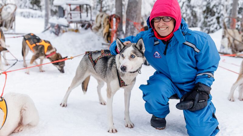 Woman traveller croucing next to a husky dog in the snow in Finland.