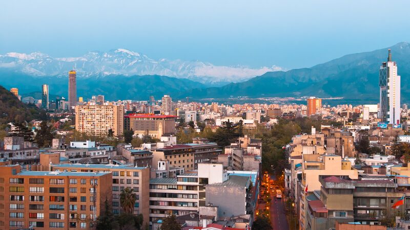 The cityscape of Santiago at twilight with a snow-capped mountain range in the distance.