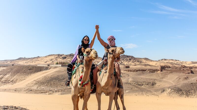 Two travellers reading camels in the Sahara Desert under a clear blue sky.